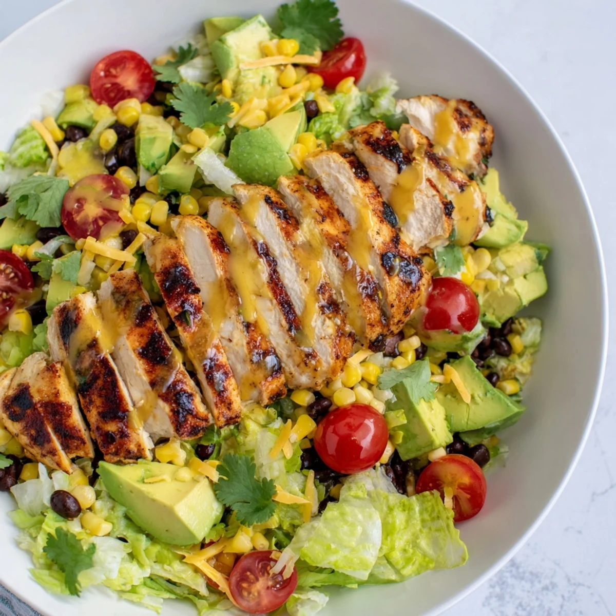 Sliced honey lime chicken arranged over a vibrant taco salad with romaine, corn, black beans, and avocado.