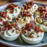 Deviled eggs with crumbled bacon and ranch dressing, garnished with fresh chives and paprika.  
