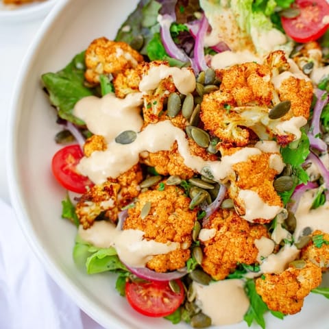 This Crispy Cauliflower Salad displays vibrant greens topped with crispy cauliflower and a delicious tahini sauce drizzle.