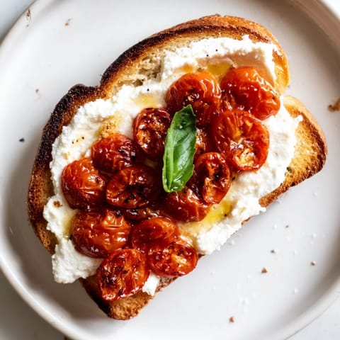Warm, caramelized tomato halves and smooth ricotta spread on a rustic slice, finished with flaky sea salt for a Mediterranean breakfast.
