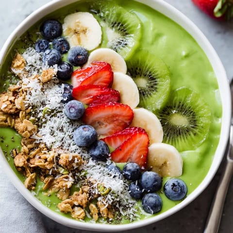 A close-up view of a creamy spinach smoothie bowl garnished with berries and shredded coconut.  