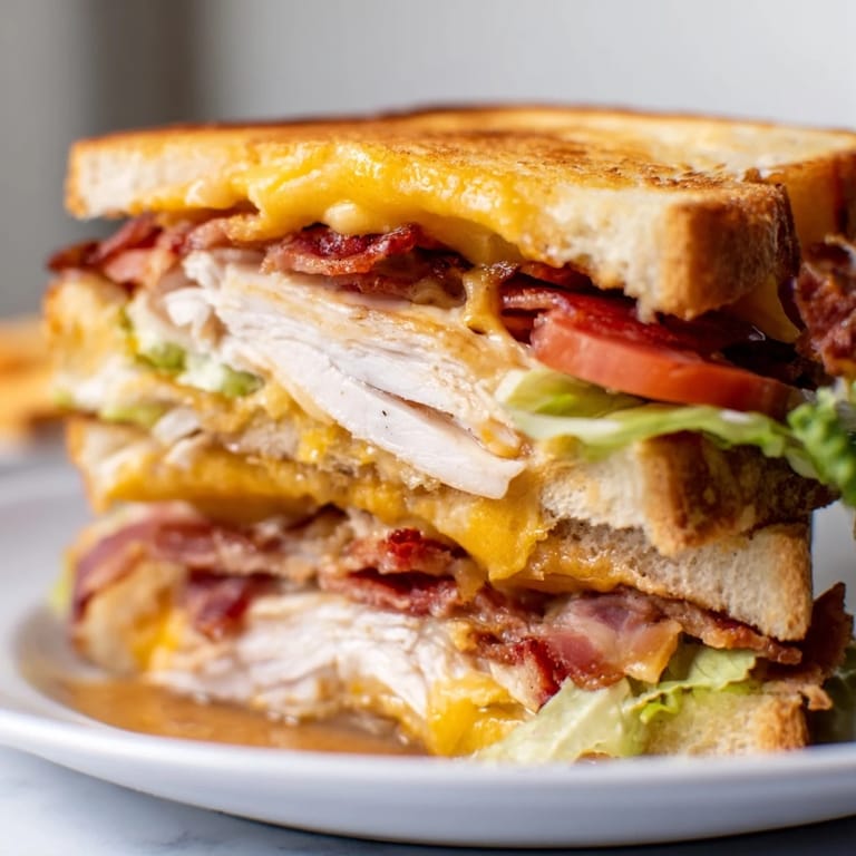 Sliced Turkey Club Grilled Cheese on a wooden board with fresh lettuce and tomato, ready to be enjoyed.