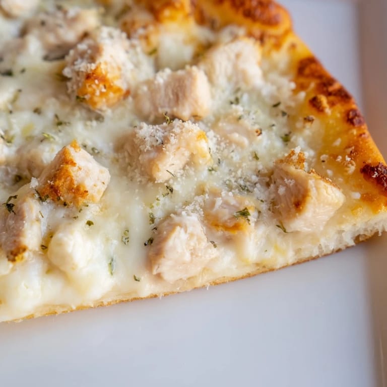 Sliced Chicken Alfredo Pizza on a wooden board, golden crust, creamy sauce, tender chicken, and fresh parsley.
